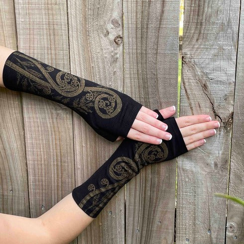 Beautiful black Merino wool gloves with a gold spiral fern print. On a womans hands, touching a fence.