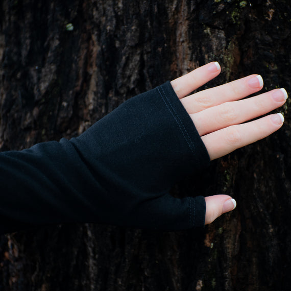 Pure black womens wool merino gloves on  hand touching a tree.
